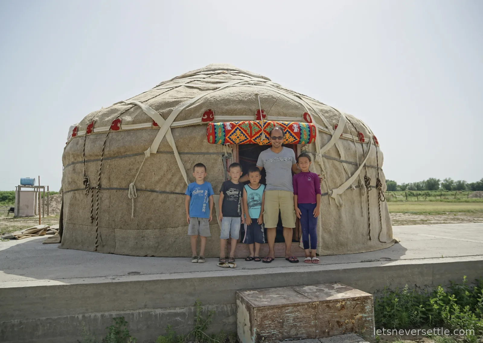Dileep standing with four children in front of a felt yurt with a colourful embroidered band above its doorway