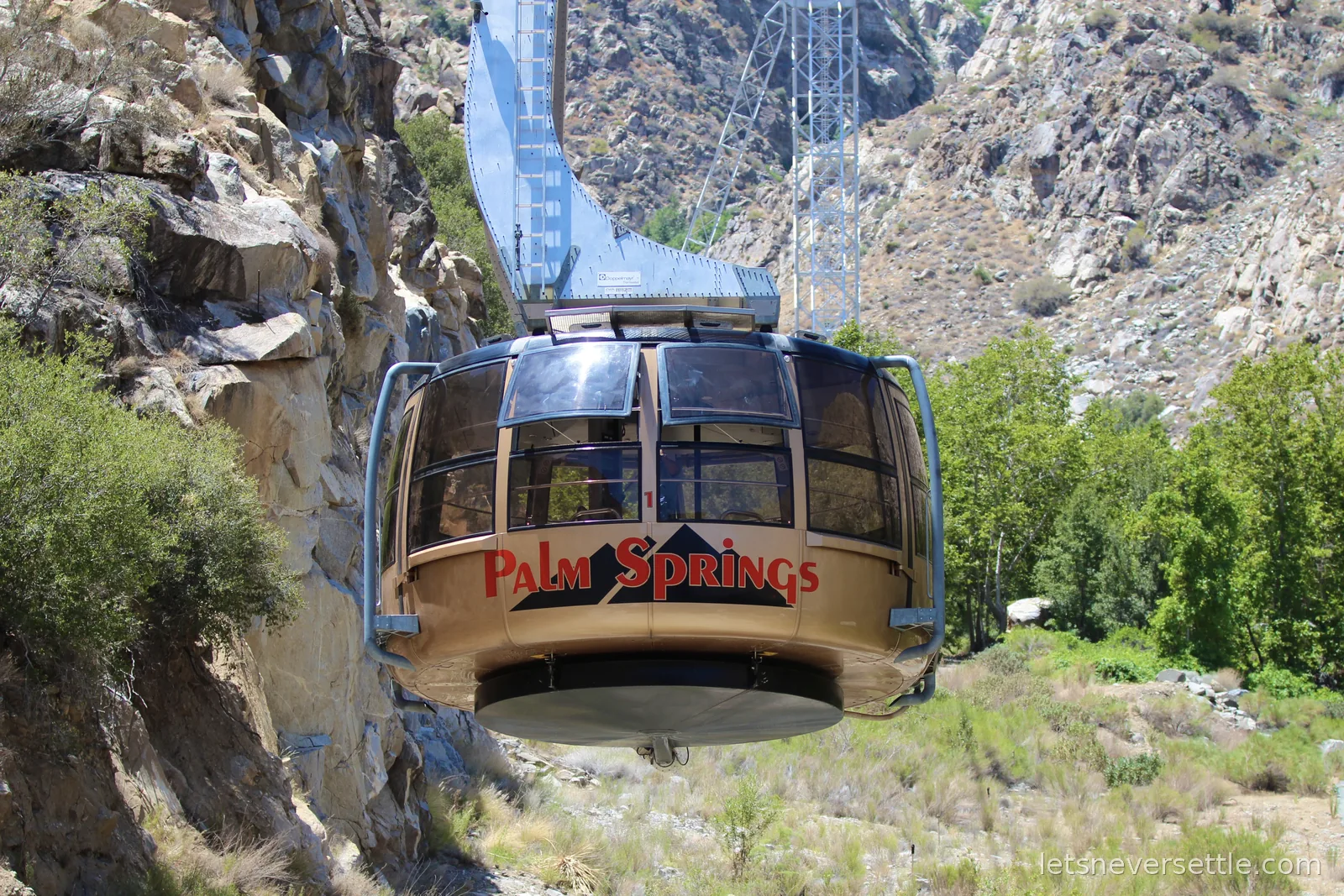 Gold Palm Springs Aerial Tramway car passing a support tower on the rocky cliffside of Chino Canyon