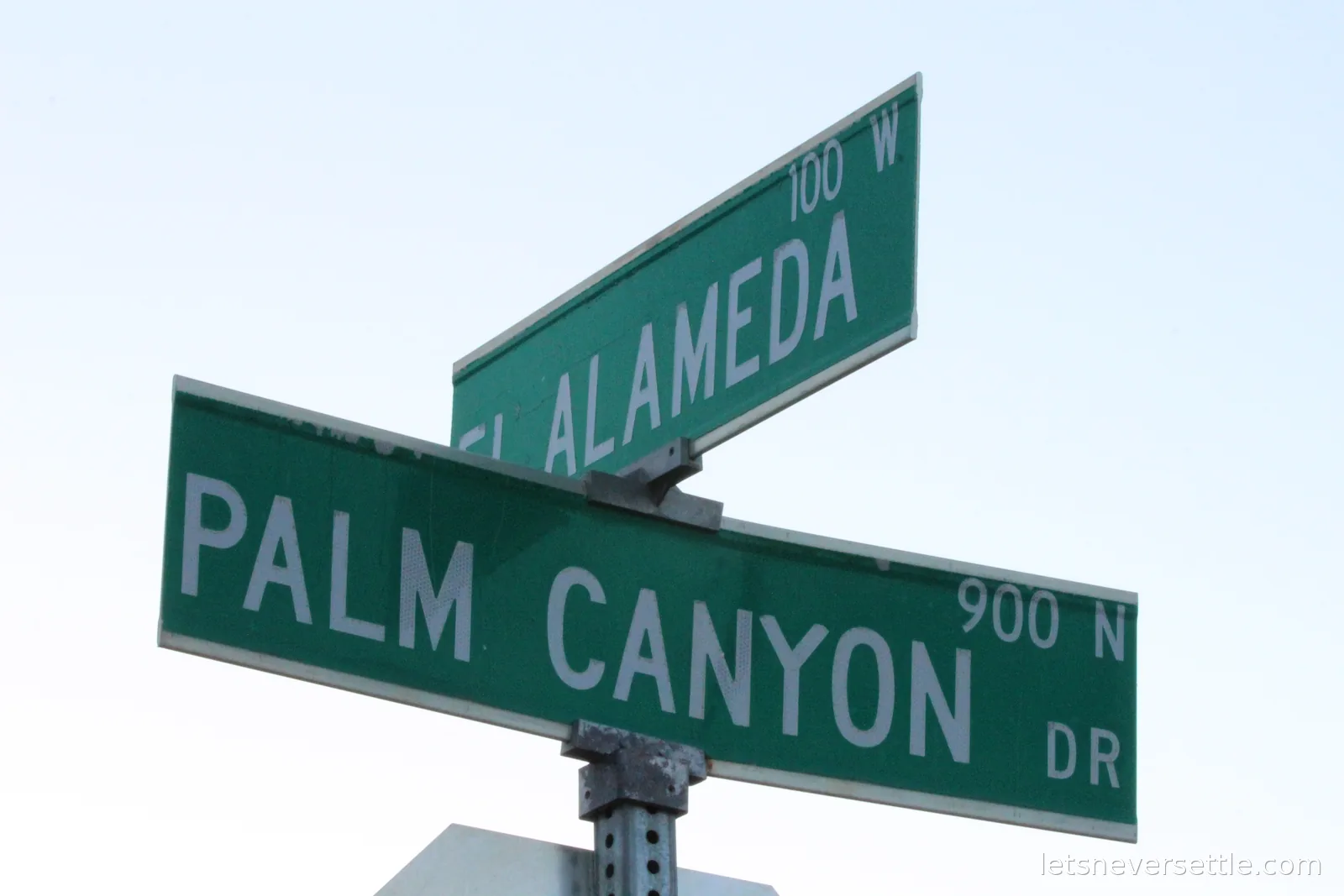 Green street signs for South Palm Canyon Drive and El Alameda against palm fronds and blue sky