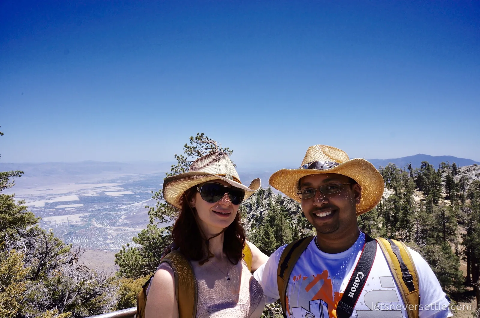 Selfie of Inga and Dileep in straw cowboy hats with pines and the pale Coachella Valley far below