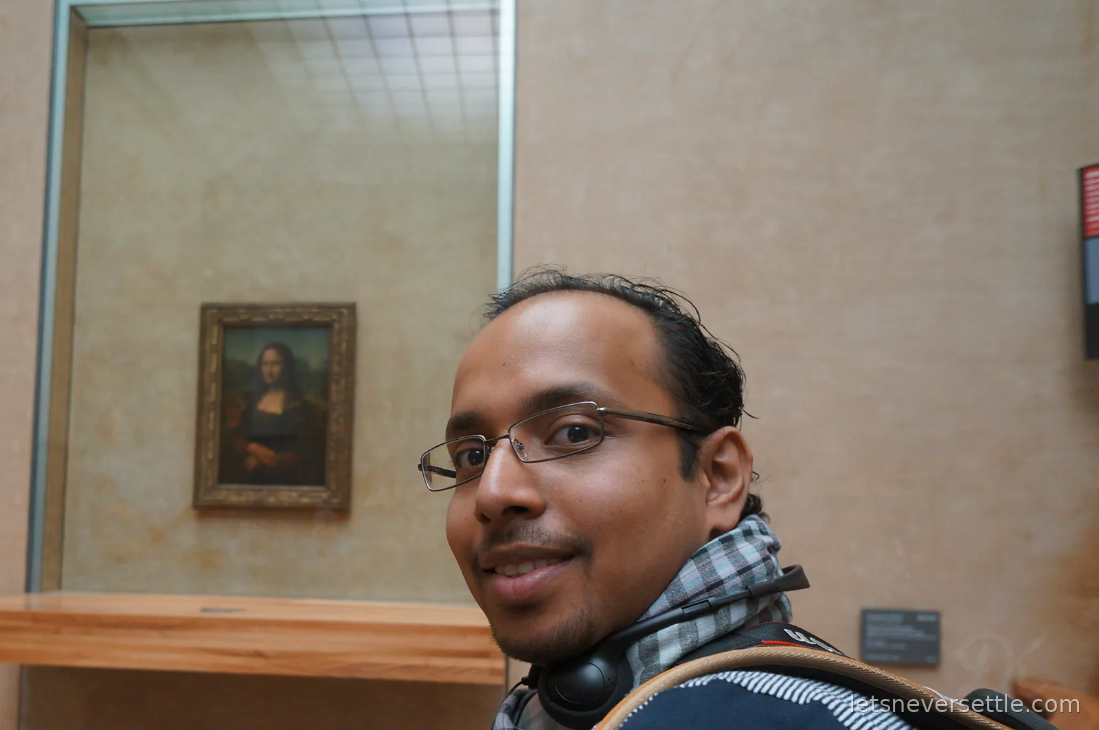 Dileep smiling in the Louvre with the Mona Lisa hanging behind glass on the wall behind him