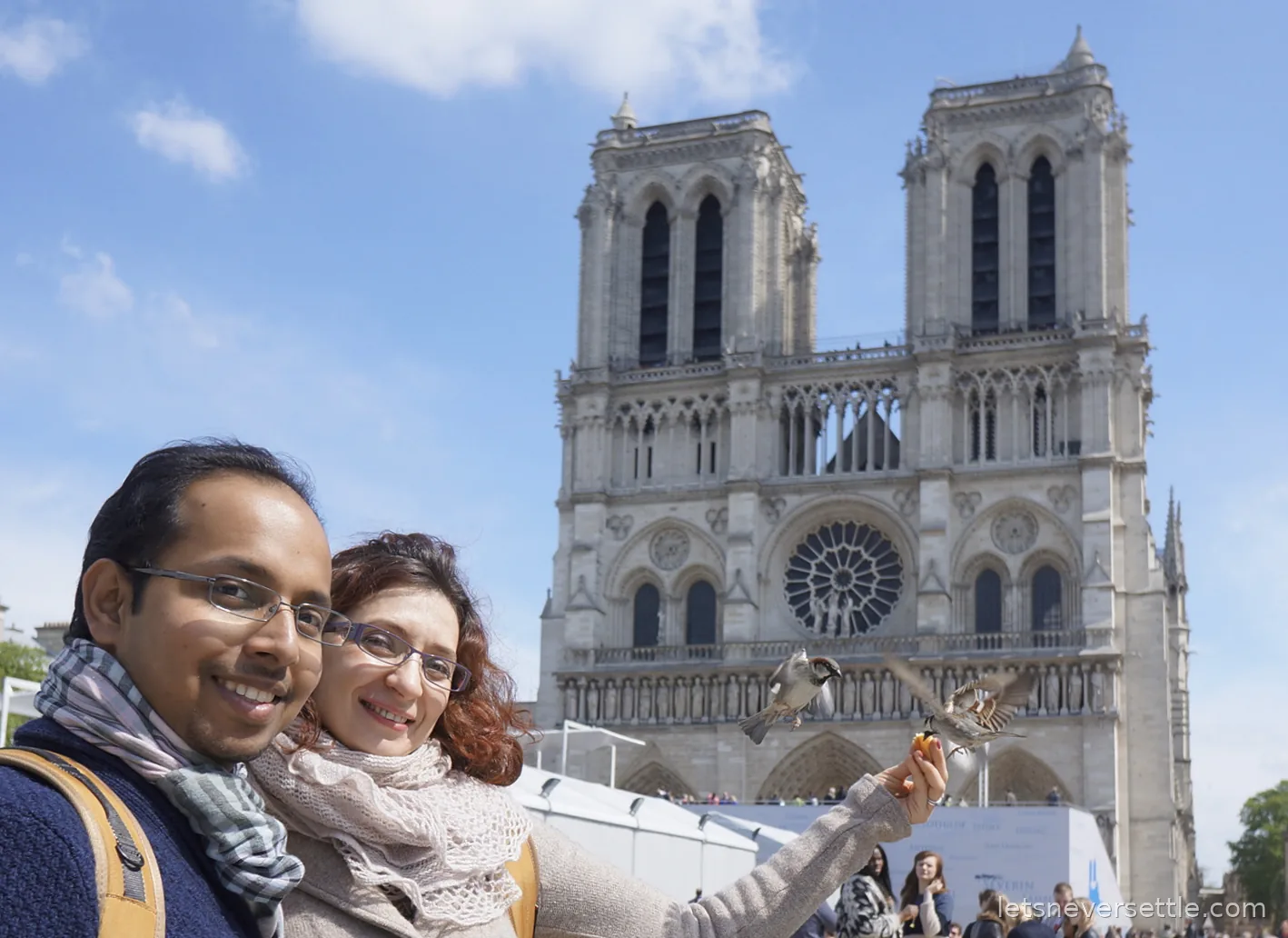 Inga and Dileep in front of the twin towers of Notre-Dame cathedral in Paris, two sparrows landing on Inga's outstretched hand