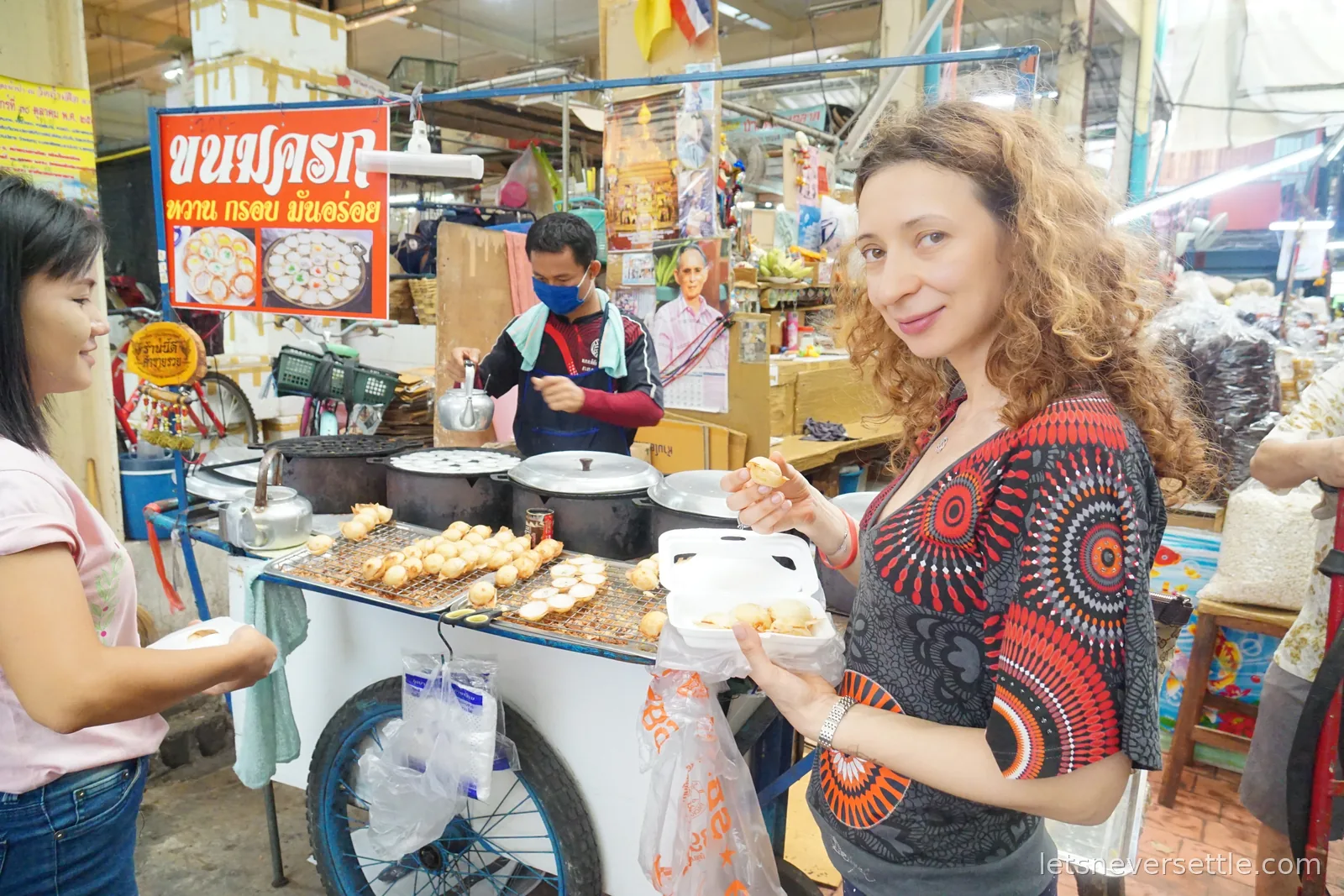 Inga holding an open box of coconut pancakes beside the cart, the masked vendor working the griddle behind her and another customer waiting with a plate
