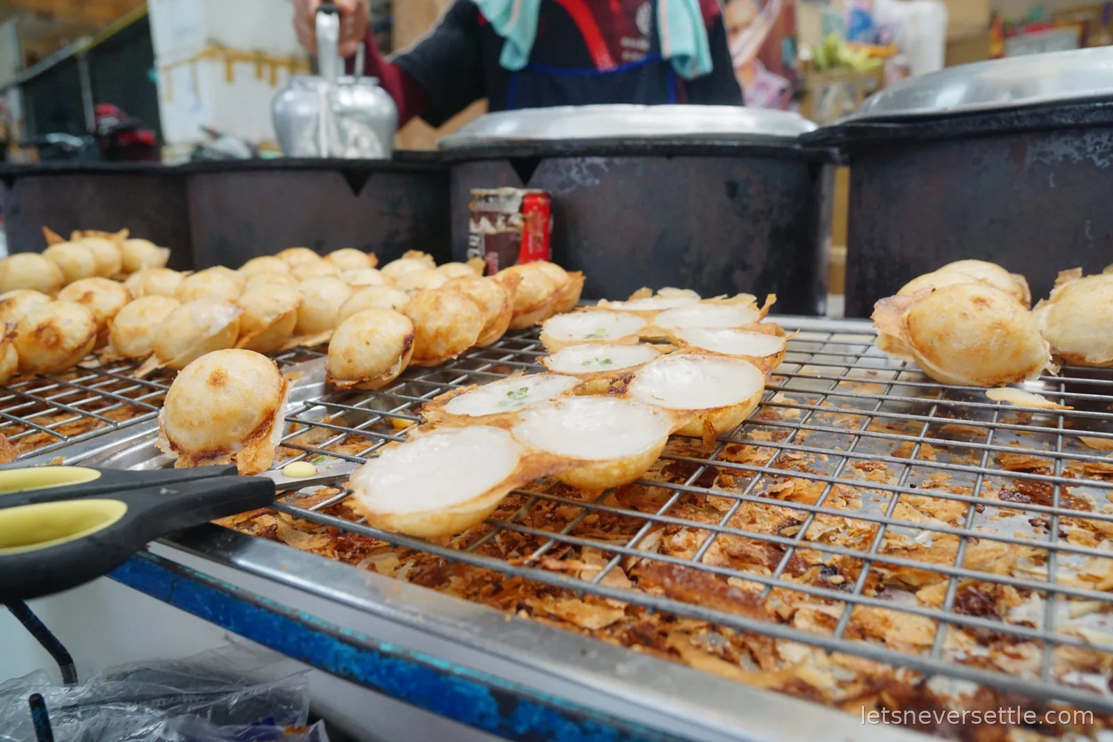 Rows of finished coconut pancakes resting on a wire rack above the griddle, some folded together in pairs with green spring onion inside