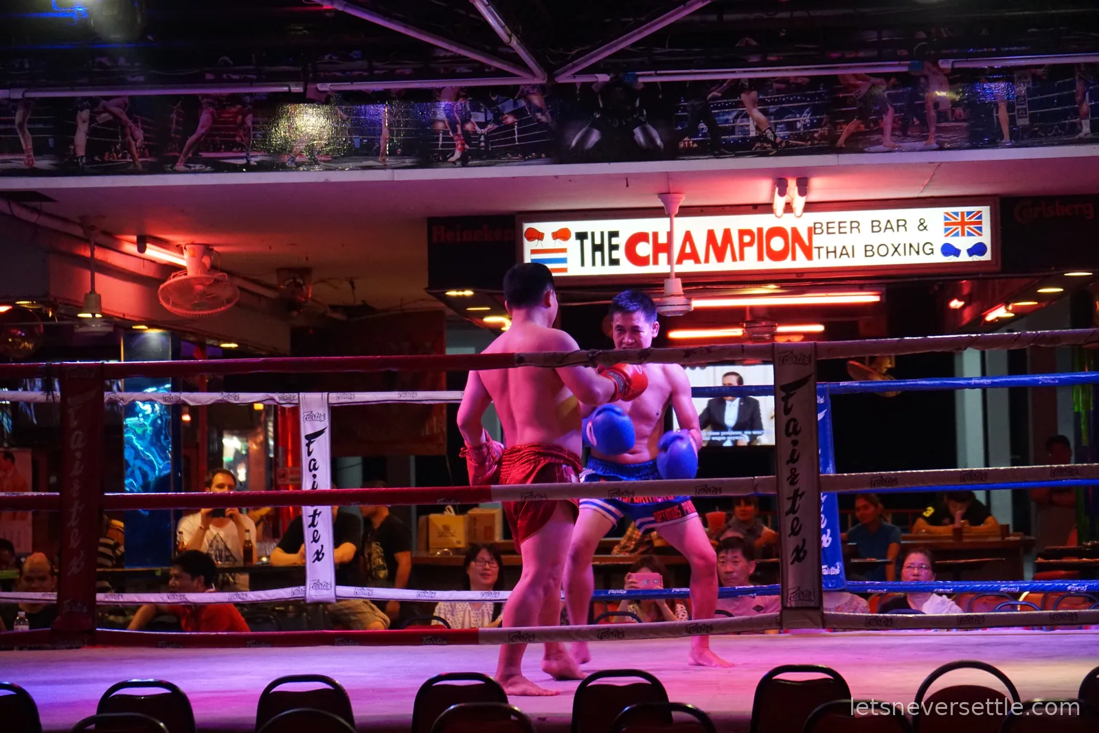 Two Muay Thai fighters facing off in the ring at The Champion beer bar in Pattaya, under a sign reading The Champion Beer Bar and Thai Boxing