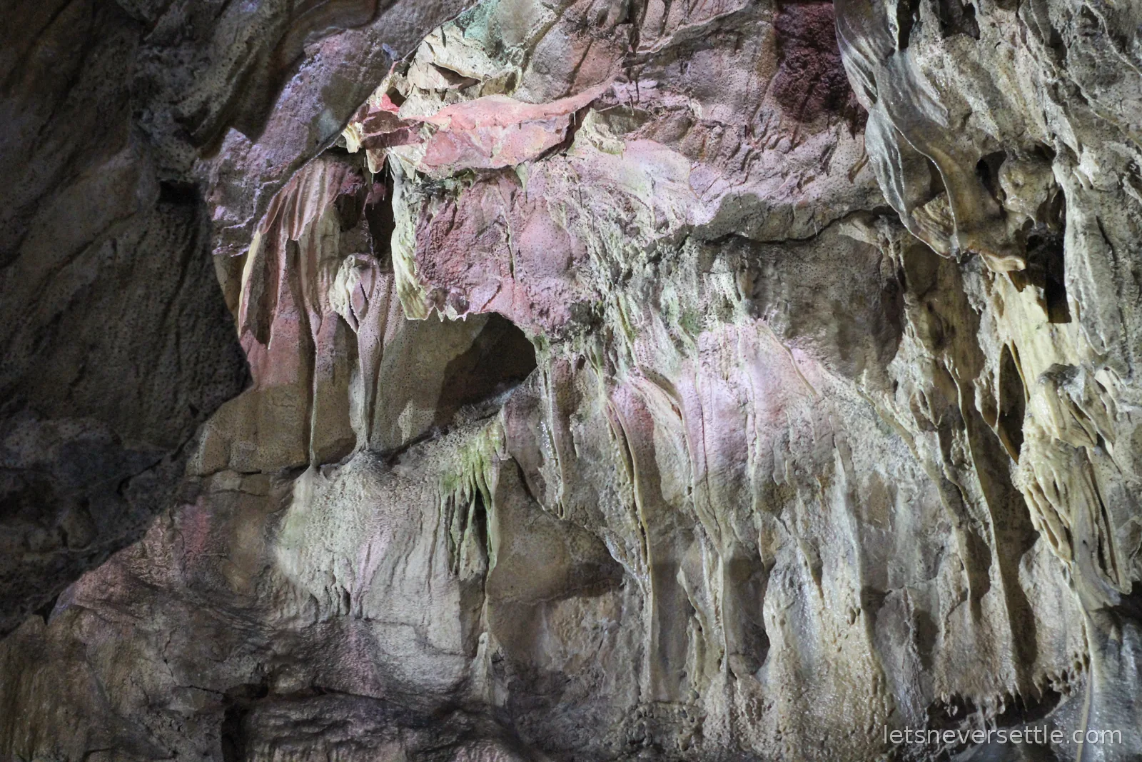 Flowstone walls inside Poole's Cavern in Buxton, streaked pink, orange and grey under the cave lighting