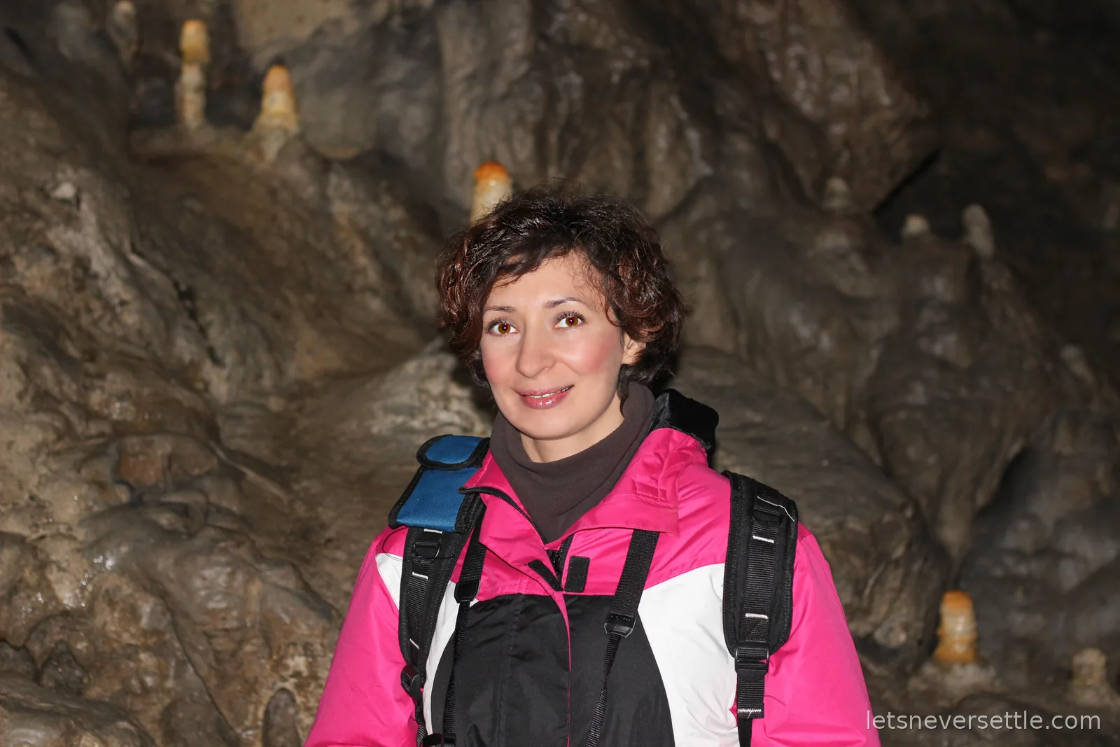 Inga in a pink jacket standing in a chamber of Poole's Cavern with stubby stalagmites rising on the rocks behind her