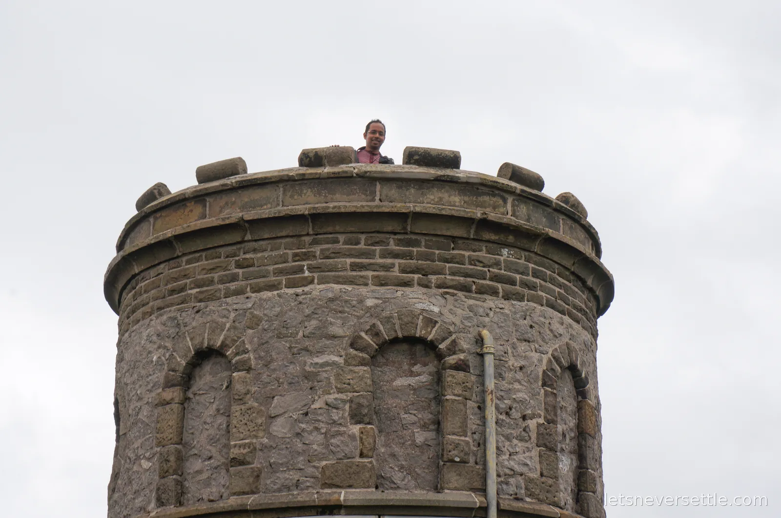 Dileep peering over the battlements at the top of Solomon's Temple tower against a white sky