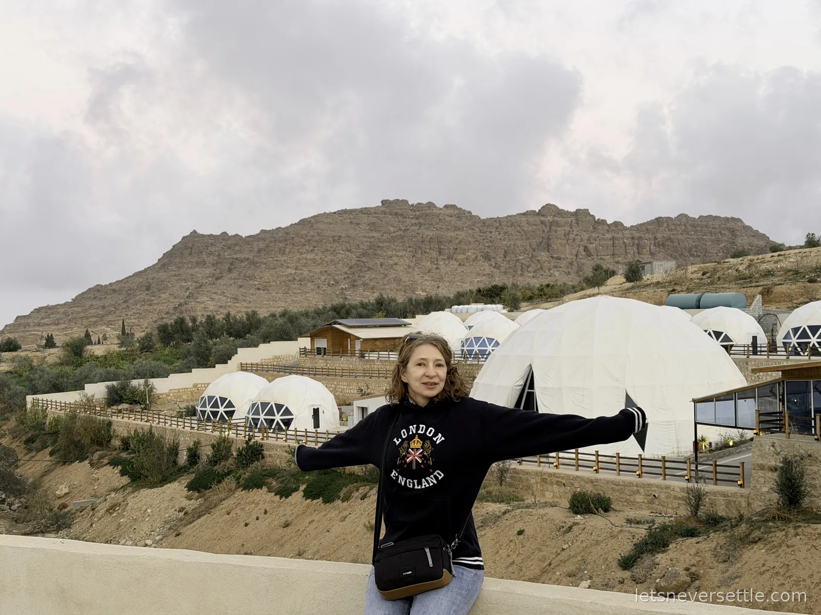 Inga standing with her arms outstretched in front of a hillside covered in white geodesic dome tents near Petra