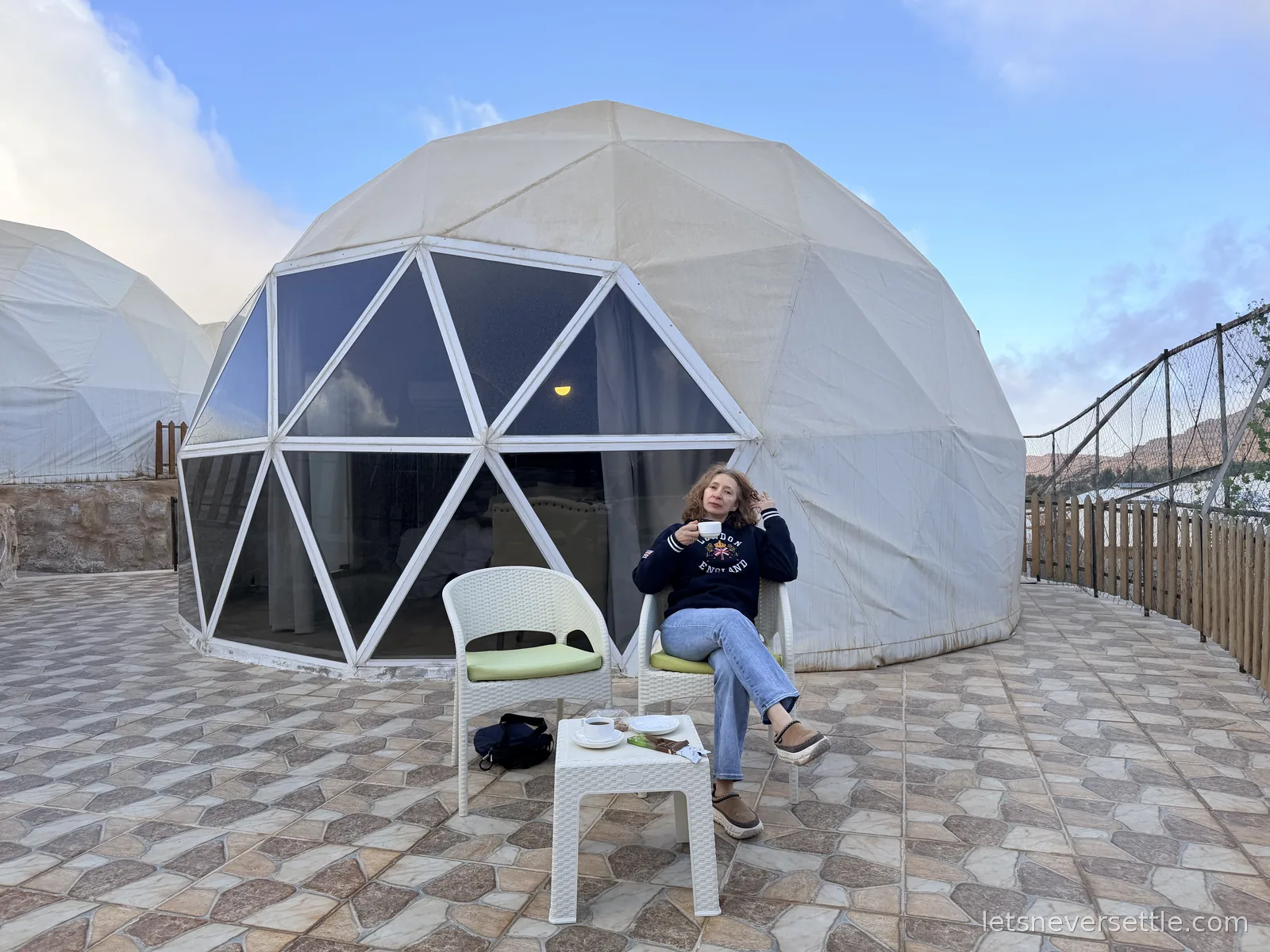 Inga drinking tea outside a white geodesic dome tent on a tiled terrace under a blue morning sky near Petra