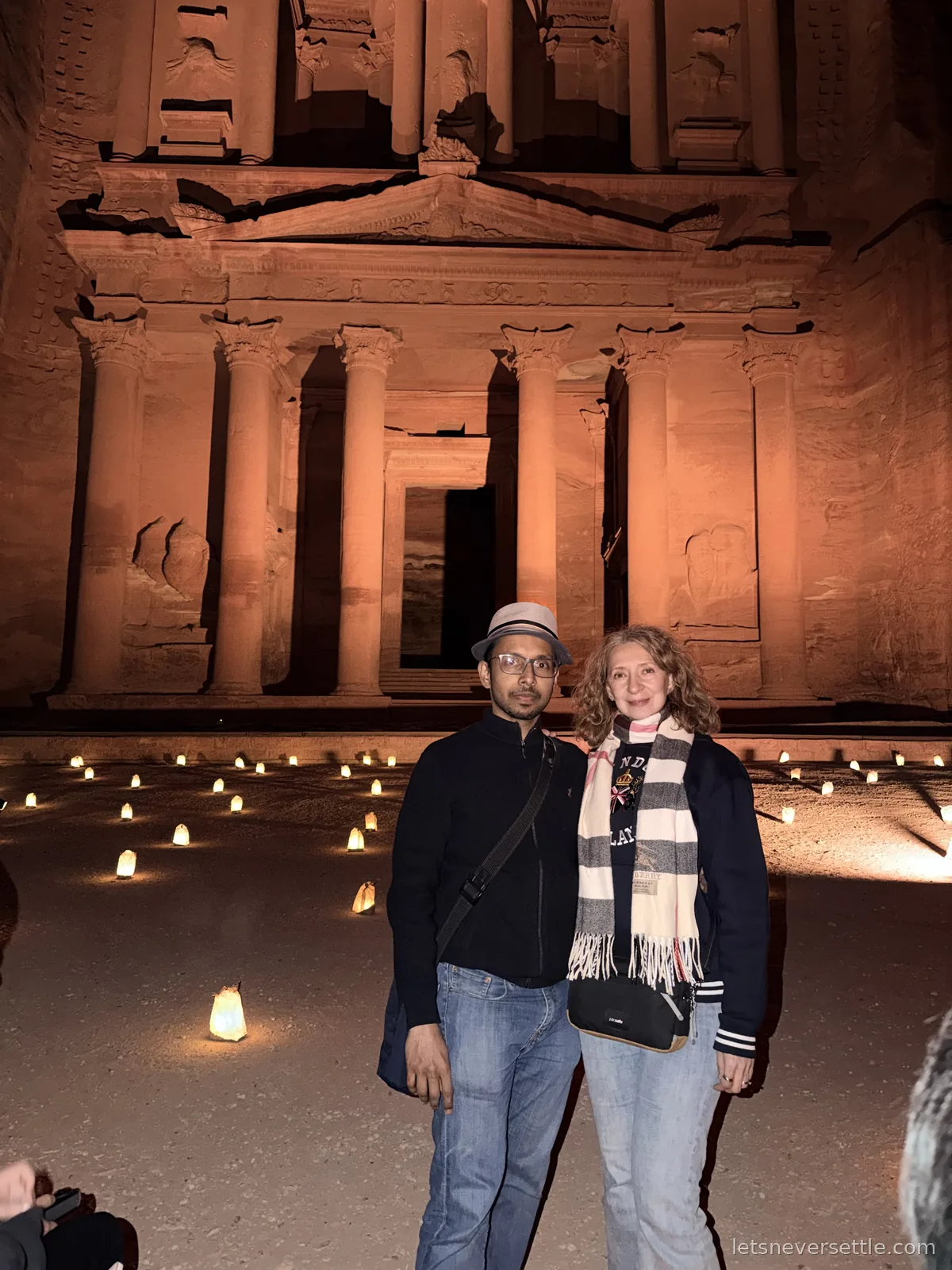 Inga and Dileep standing in coats and scarves in front of the candlelit Treasury at Petra during the Petra by Night show