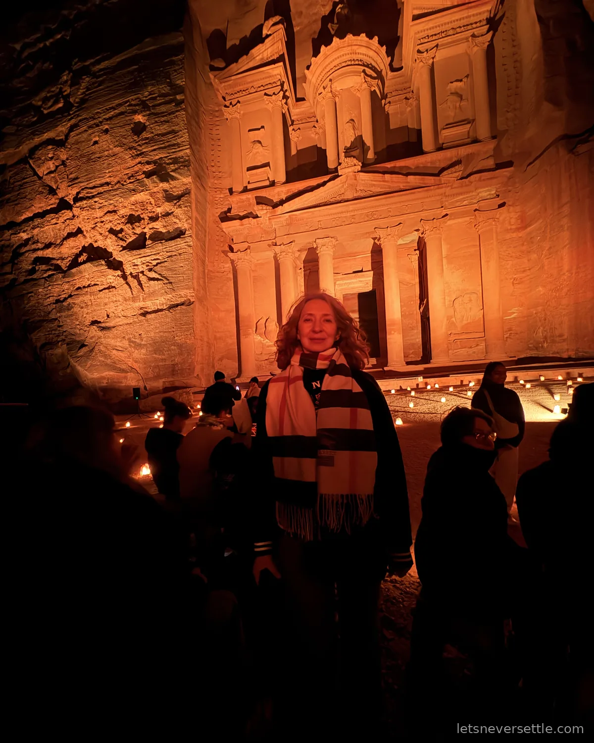 Inga in a striped scarf standing in front of the Treasury at night, its facade glowing orange above rows of candles