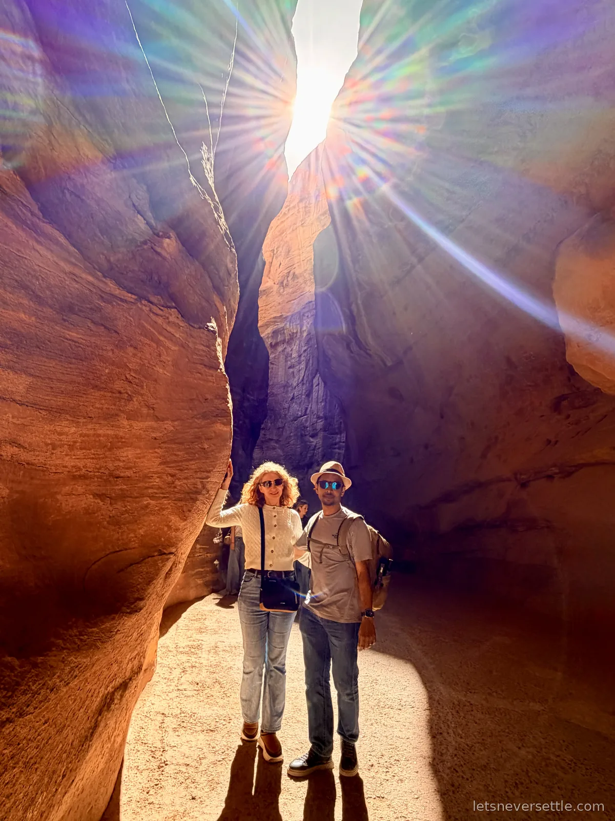 Inga and Dileep standing in the narrow Siq canyon at Petra with the sun bursting through the gap in the rock walls above