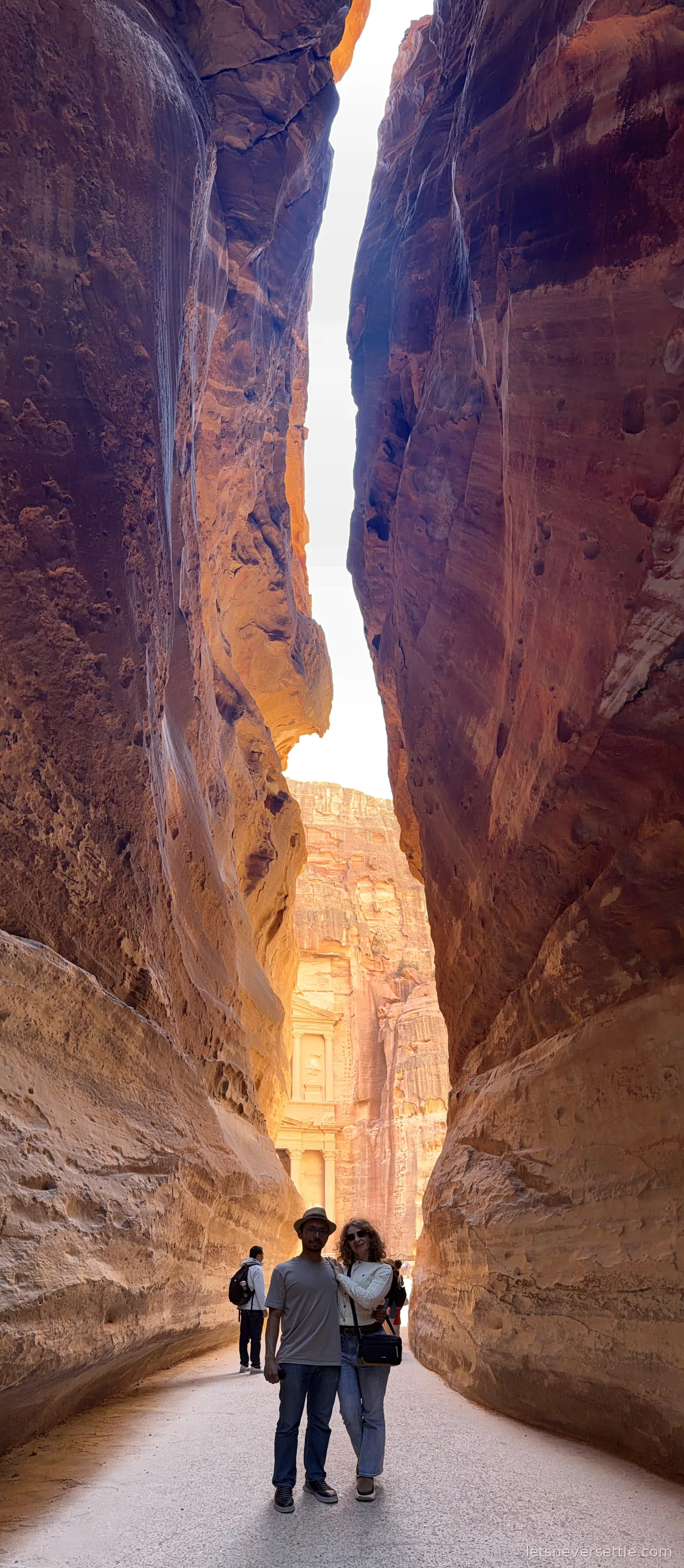 Vertical panorama of the narrow Siq canyon at Petra with the sunlit Treasury facade appearing in the gap at the far end