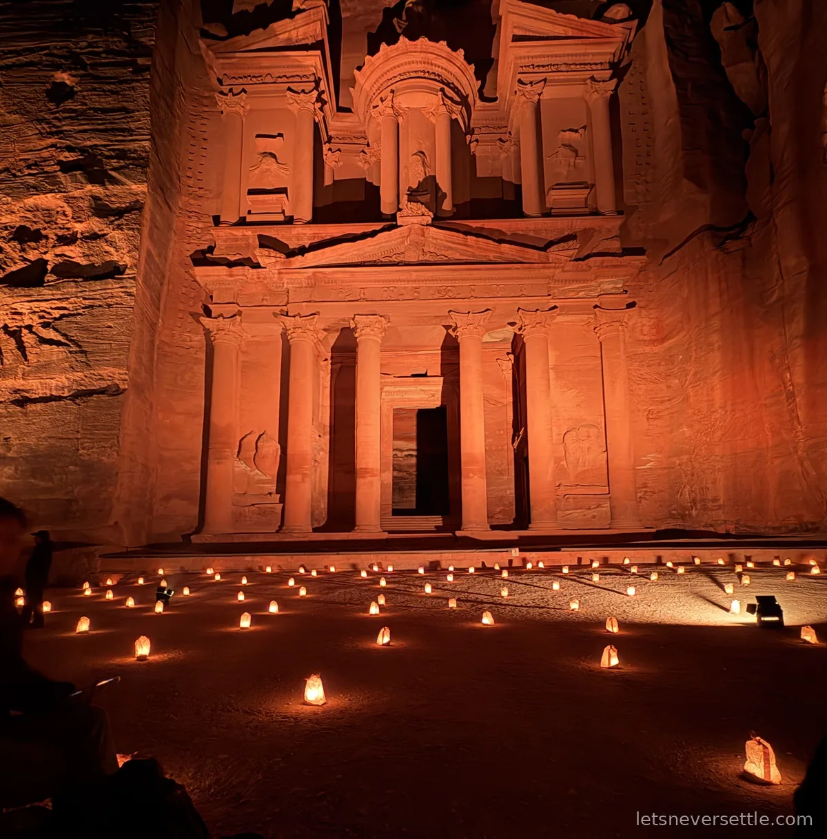 The Treasury at Petra glowing orange at night above hundreds of paper candle lanterns laid out in rows across the sand
