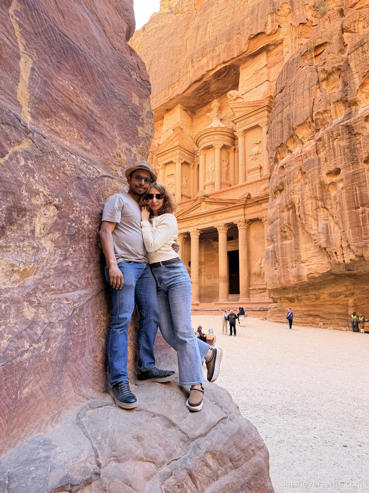 Inga and Dileep leaning against a boulder in the sunlit plaza in front of the Treasury at Petra