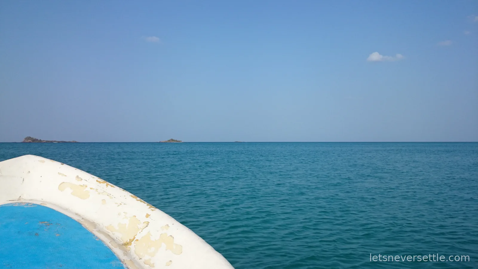 The white bow of a small boat on flat turquoise sea, the rocky islets of Pigeon Island low on the horizon