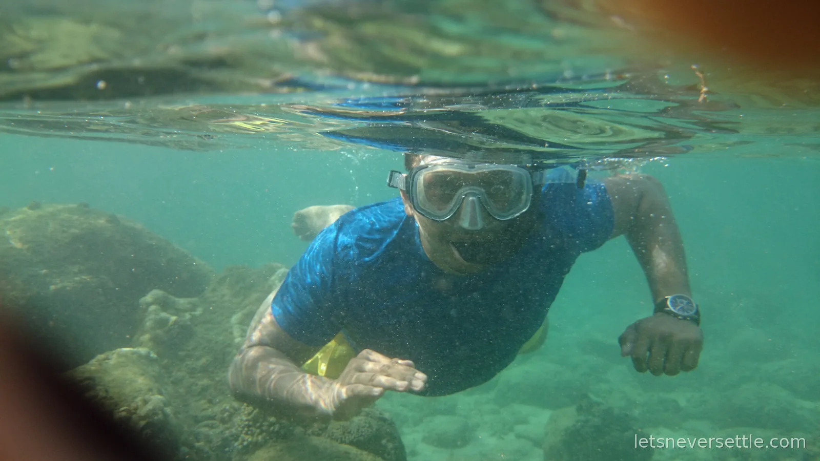 Dileep in a snorkel mask swimming just under the surface, coral rocks below him
