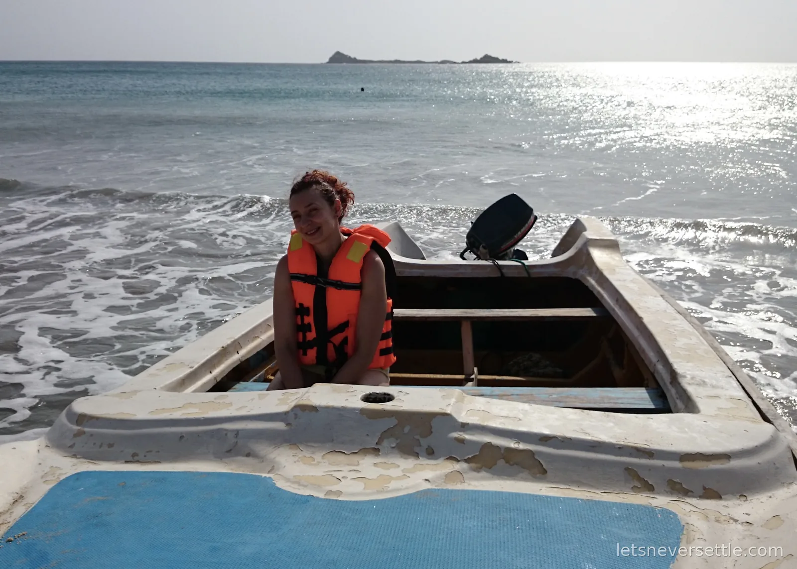 Inga in an orange life jacket sitting in an open boat in the surf, a rocky islet out at sea behind her
