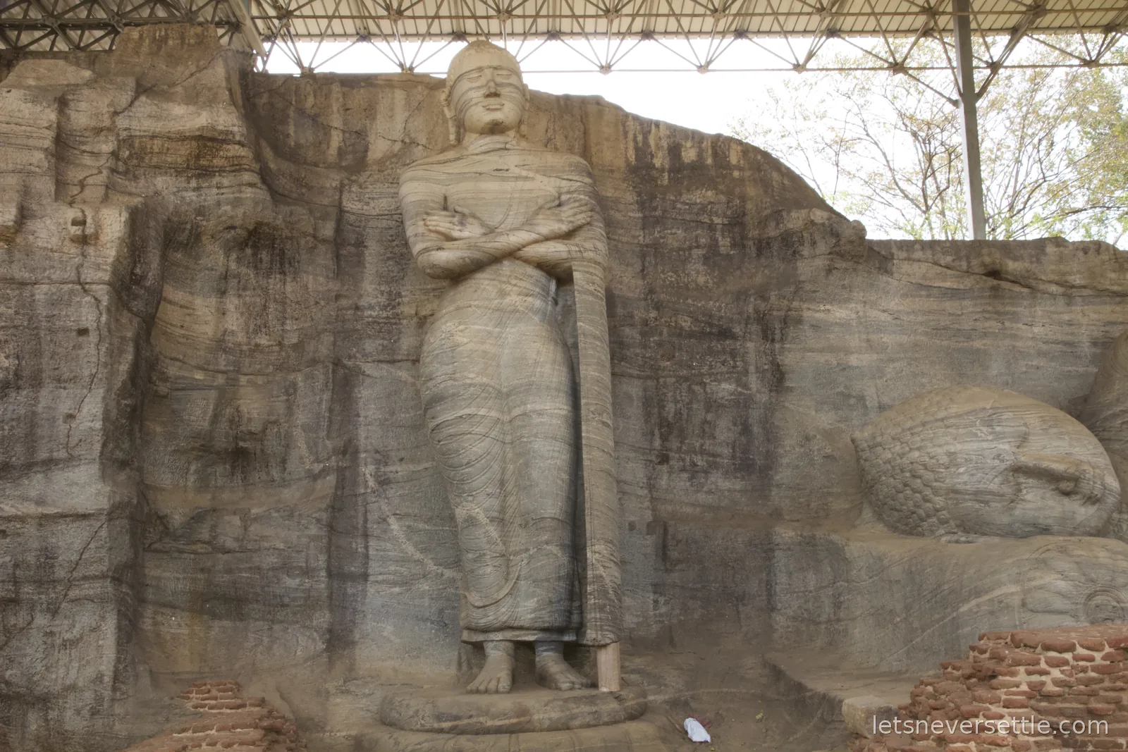 The standing Buddha of Gal Vihara carved from streaked granite with arms folded, the head of the reclining Buddha visible to the right