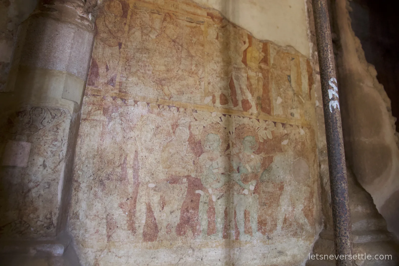 Faded centuries-old murals of robed figures painted on a plastered shrine wall beside a carved stone column