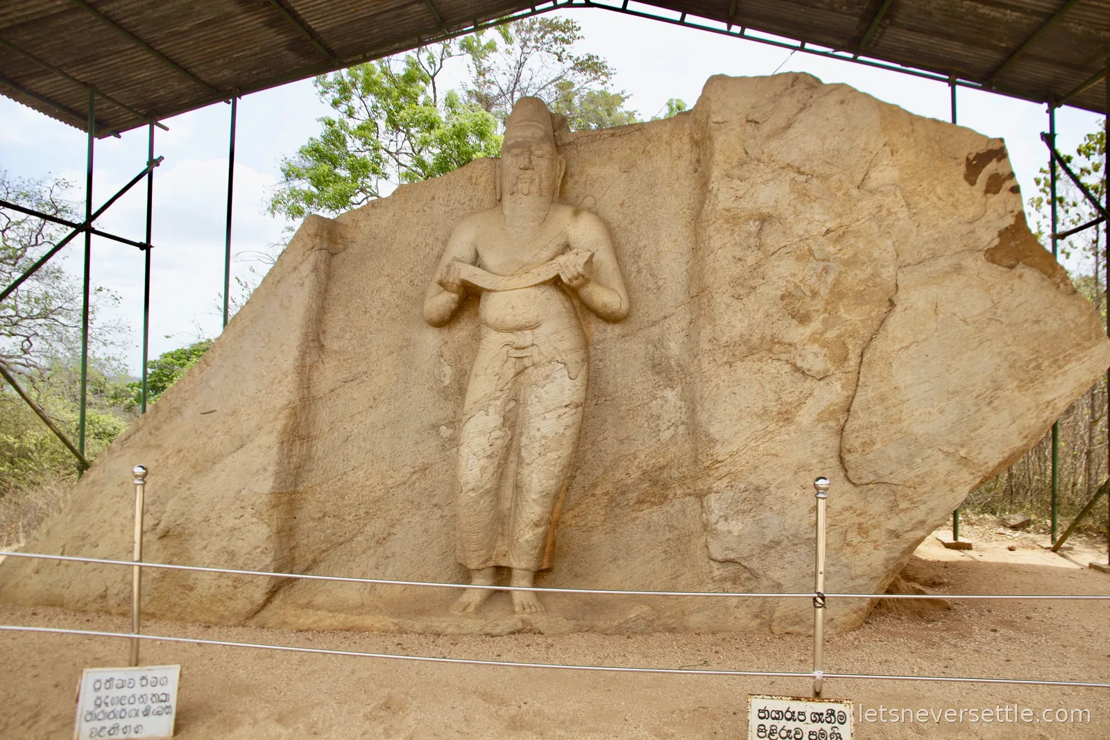 Rock-cut statue of a bearded robed figure holding a manuscript, carved in high relief from a granite boulder at Polonnaruwa