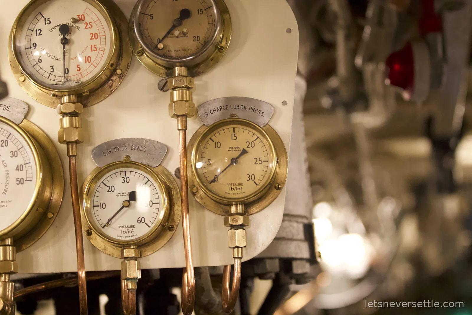 A panel of brass pressure gauges with copper piping inside the submarine HMS Alliance, one labelled S/Charge Lub Oil Press