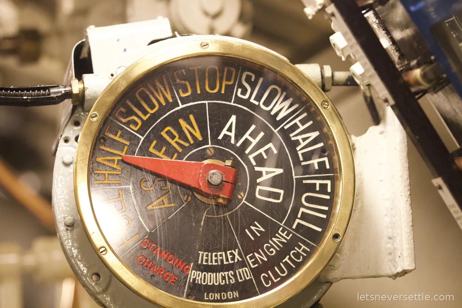 A brass engine telegraph on HMS Alliance made by Teleflex Products Ltd London, its red handle pointing among settings for slow, half and full ahead and astern