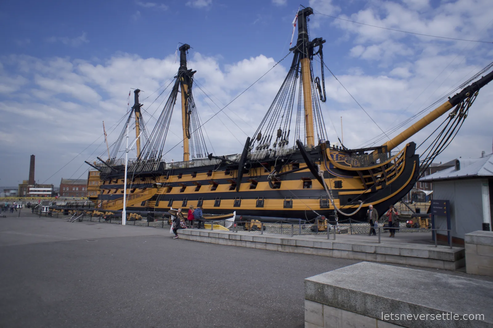 HMS Victory in dry dock at Portsmouth Historic Dockyard, three masts rigged and hull painted in black and yellow bands