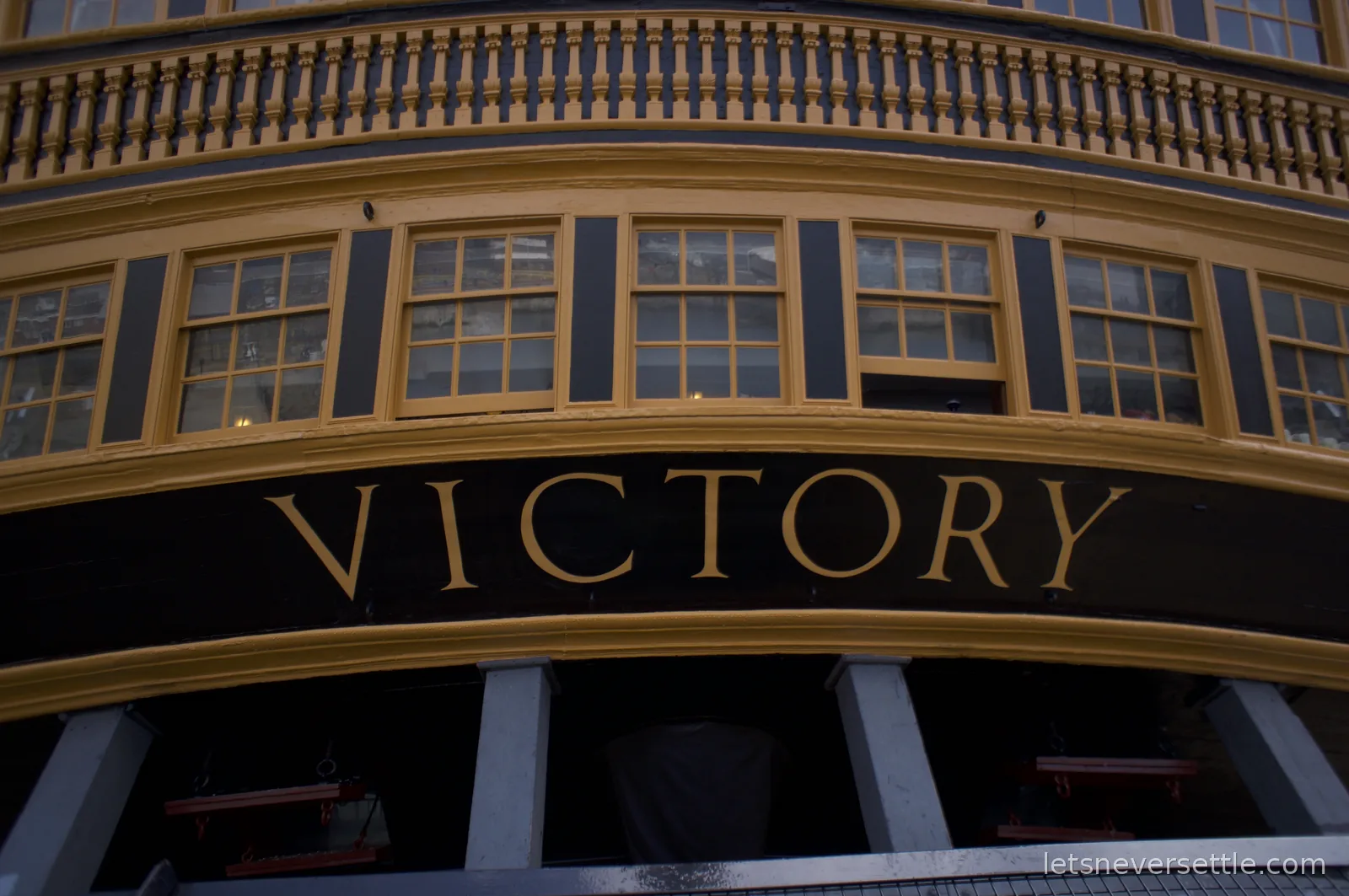 The stern of HMS Victory with the name VICTORY painted in gold letters beneath rows of gallery windows
