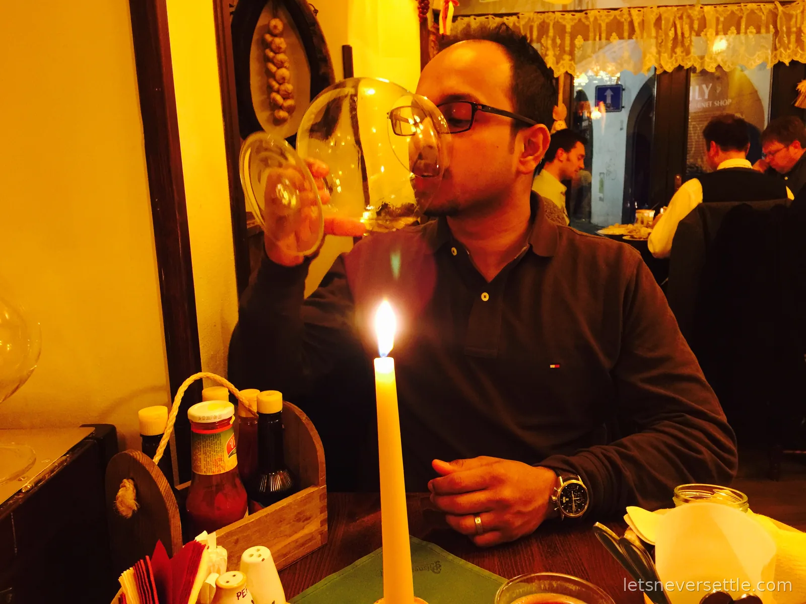 Dileep drinking from an enormous balloon wine glass by candlelight in a cosy Prague tavern