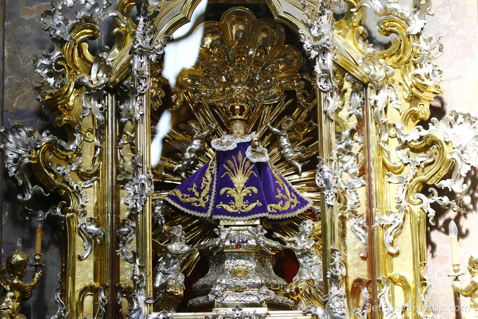 The Infant Jesus of Prague statue in a purple and gold embroidered mantle and crown, framed by a gilded baroque altar