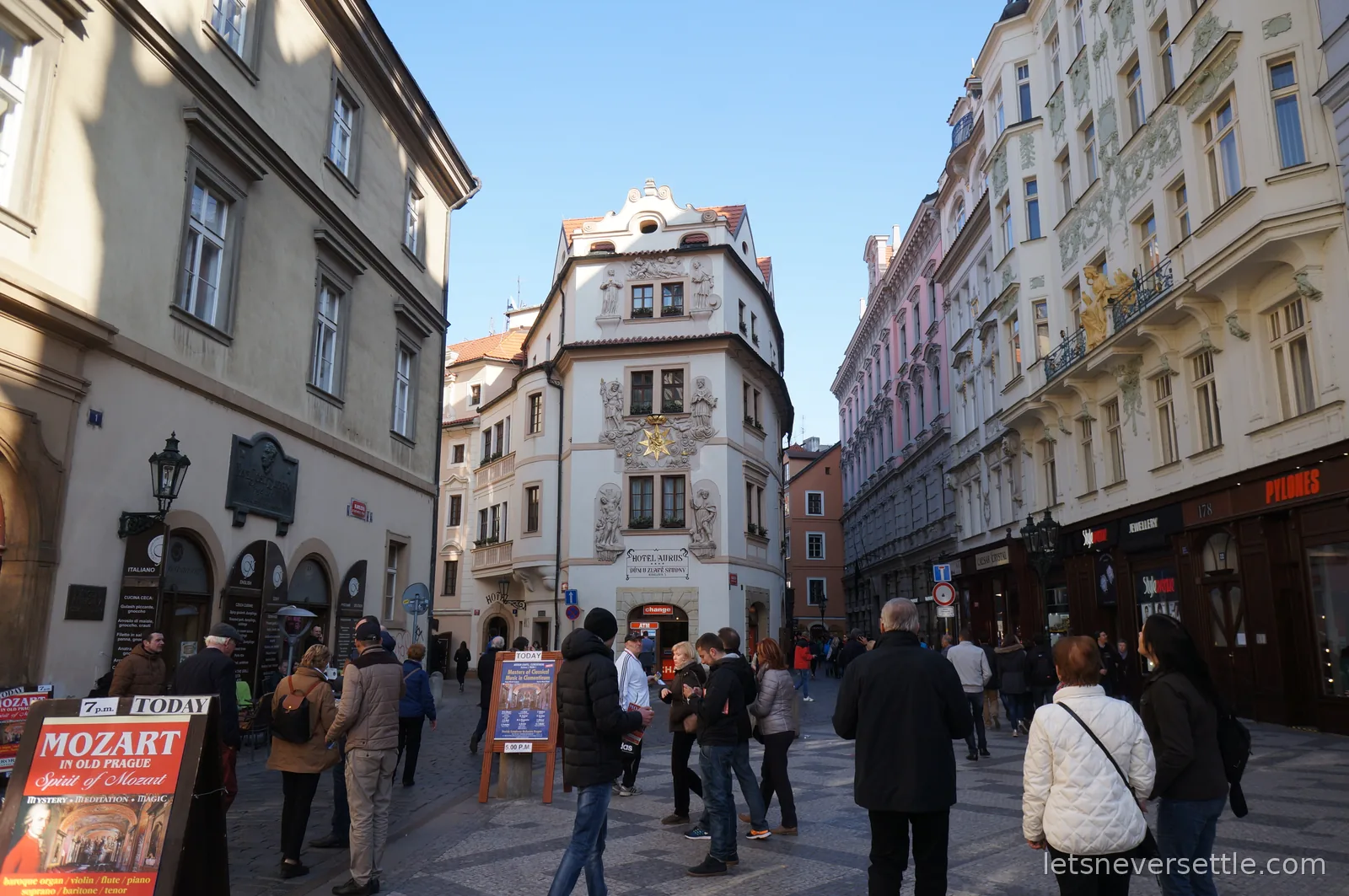 A cobbled Old Town street in Prague between ornate facades, with sandwich boards advertising Mozart and classical concerts