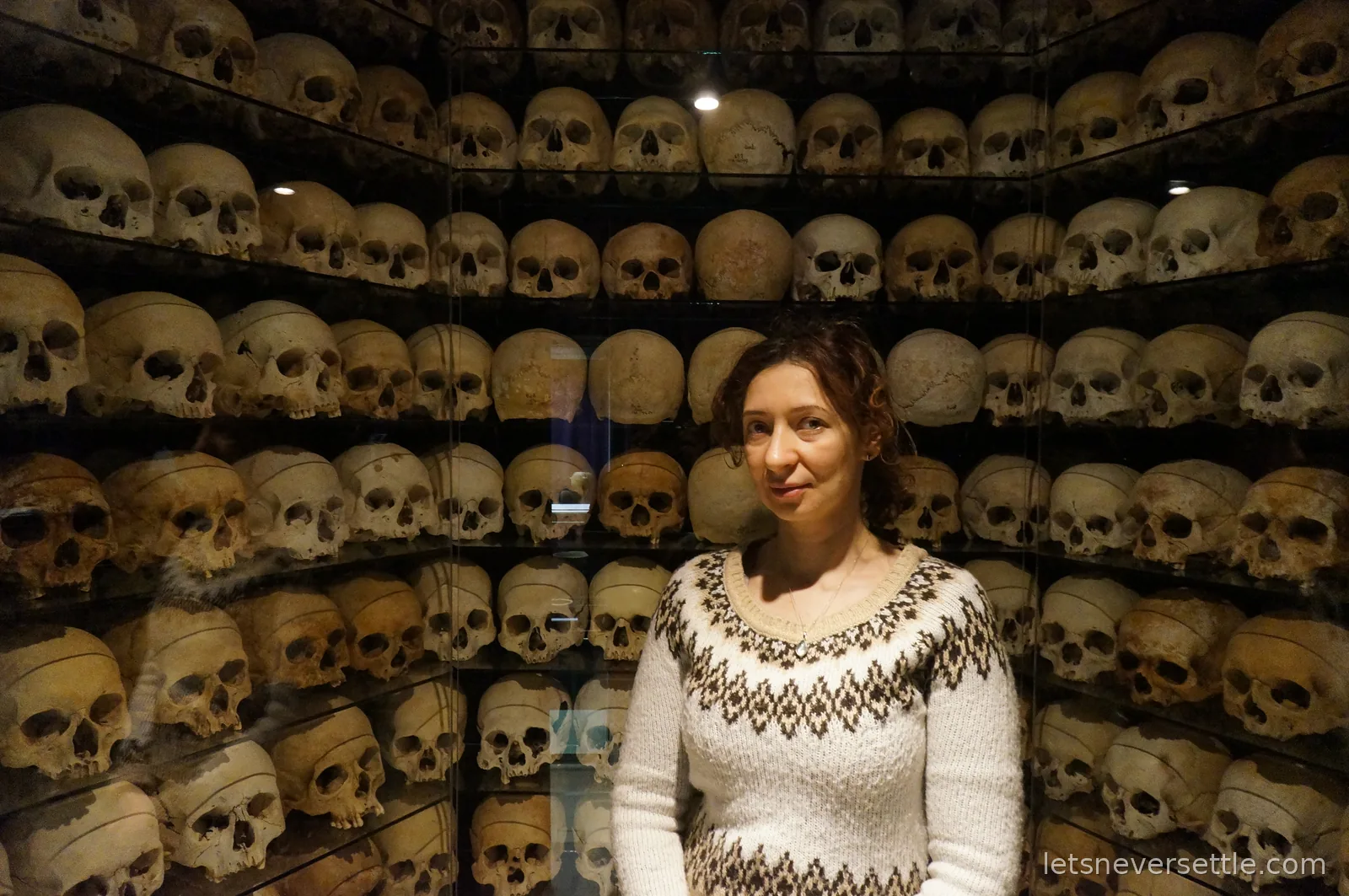 Inga in front of a glass case holding shelves of skulls at a museum in Prague