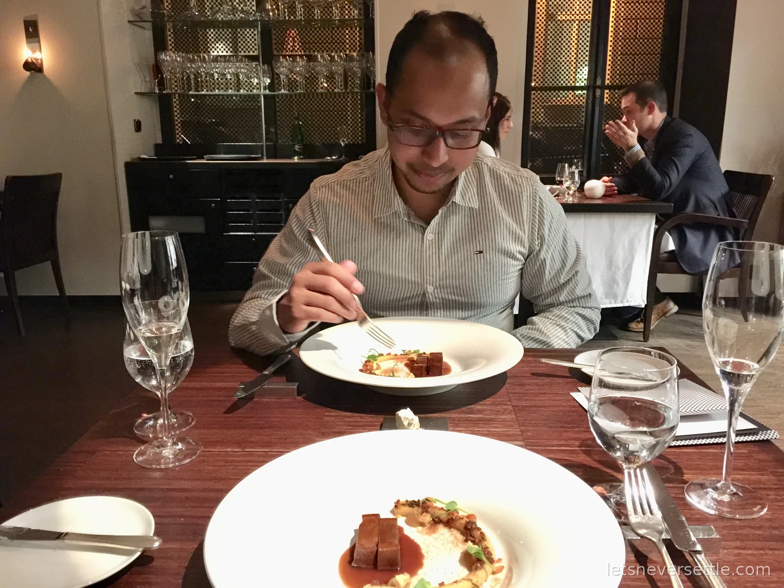 Dileep in a striped shirt lifting a fork over a plated tasting course in a smart Prague restaurant