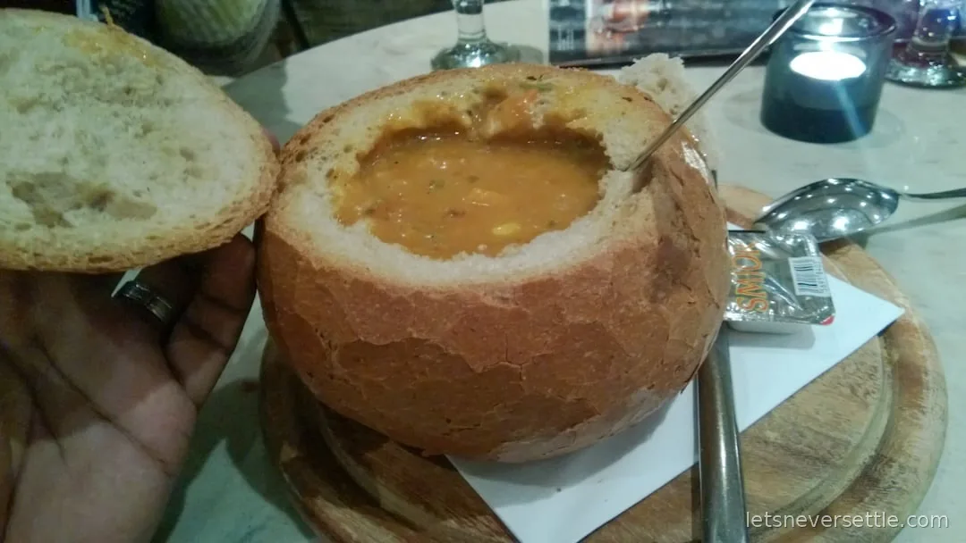 Thick soup served inside a hollowed round loaf of bread with the lid balanced beside it