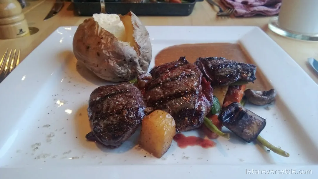 Grilled steak pieces with baked potato, mushrooms and vegetables on a white plate