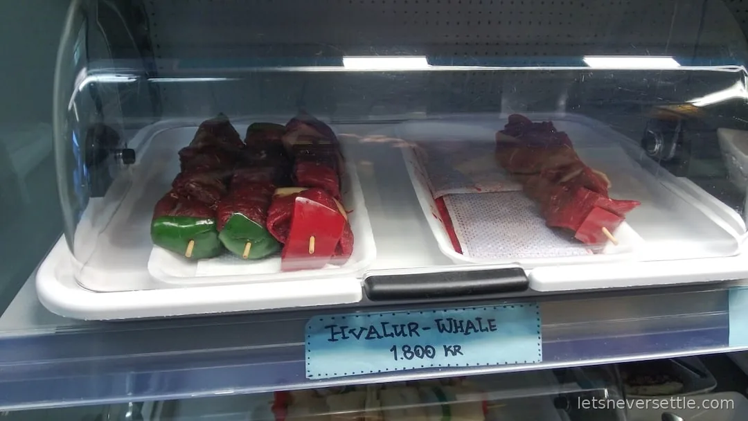 Whale meat skewers in a refrigerated display case with a handwritten sign reading Hvalur, Whale, 1800 kronur