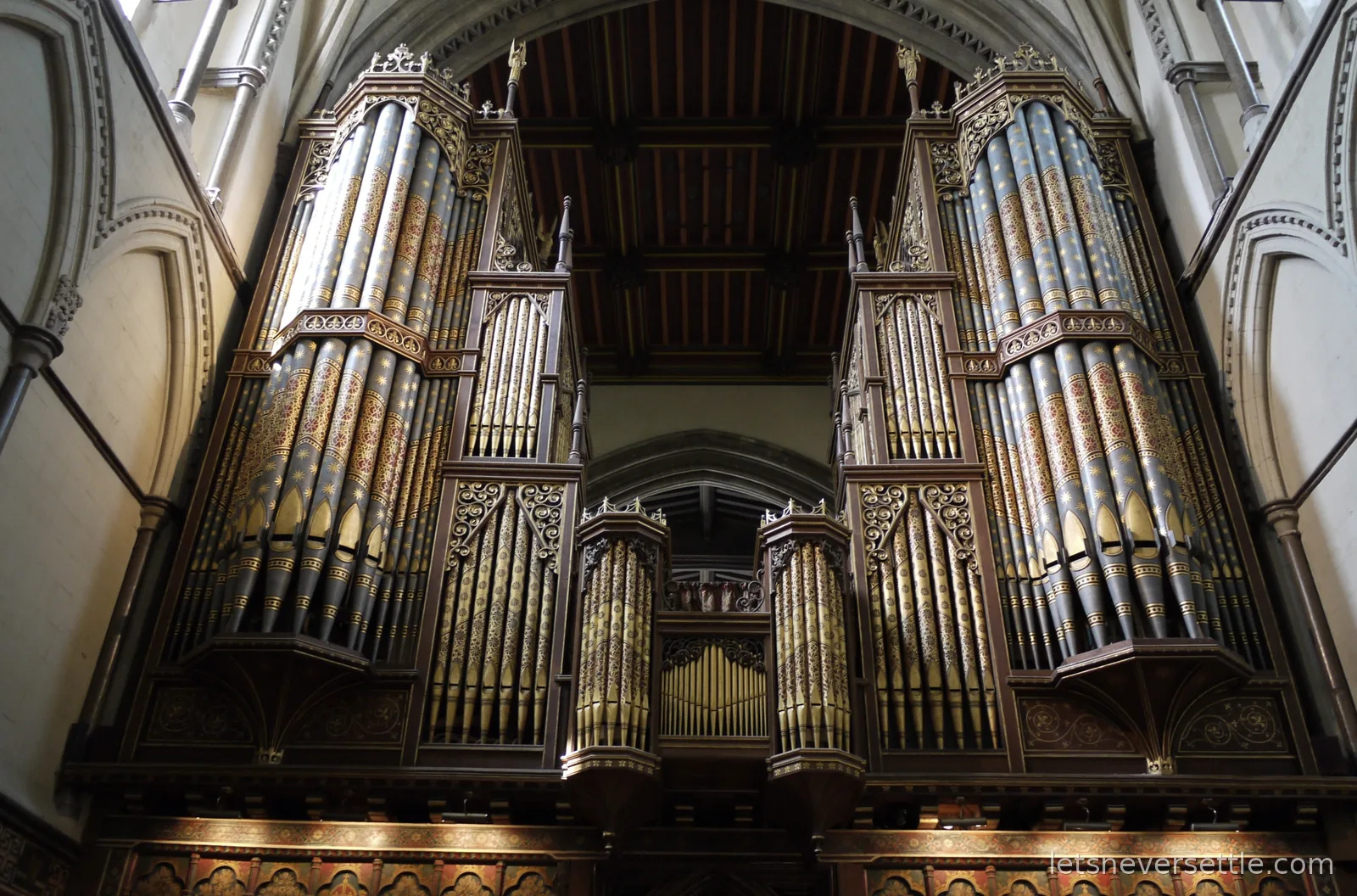 The organ of Rochester Cathedral, its pipes stencilled in gold and red beneath a painted wooden ceiling