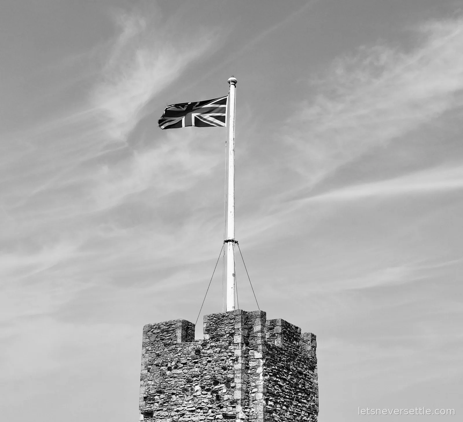 The Union Jack flying from a white flagpole on a battlemented tower of Rochester Castle, in black and white