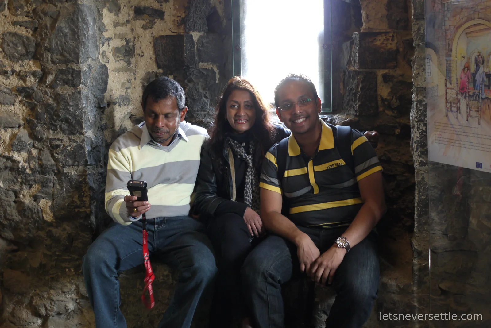 Dileep with his parents squeezed together in the same stone window recess, his father looking down at a camera