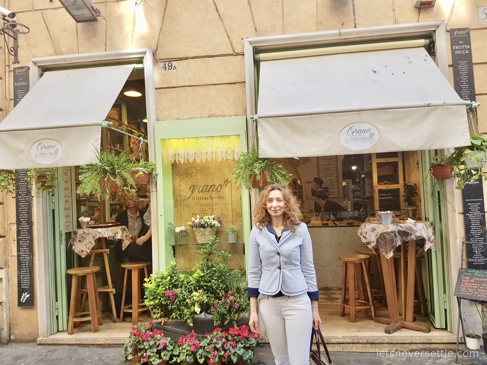 Inga outside a small bakery with a mint green shopfront, white awnings, hanging ferns and flower pots on the pavement