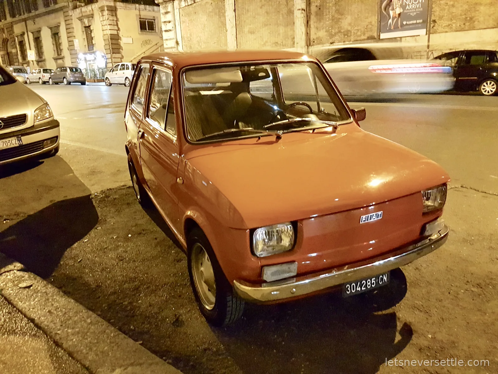 A small orange Fiat 126 parked at the kerb on a Rome street at night