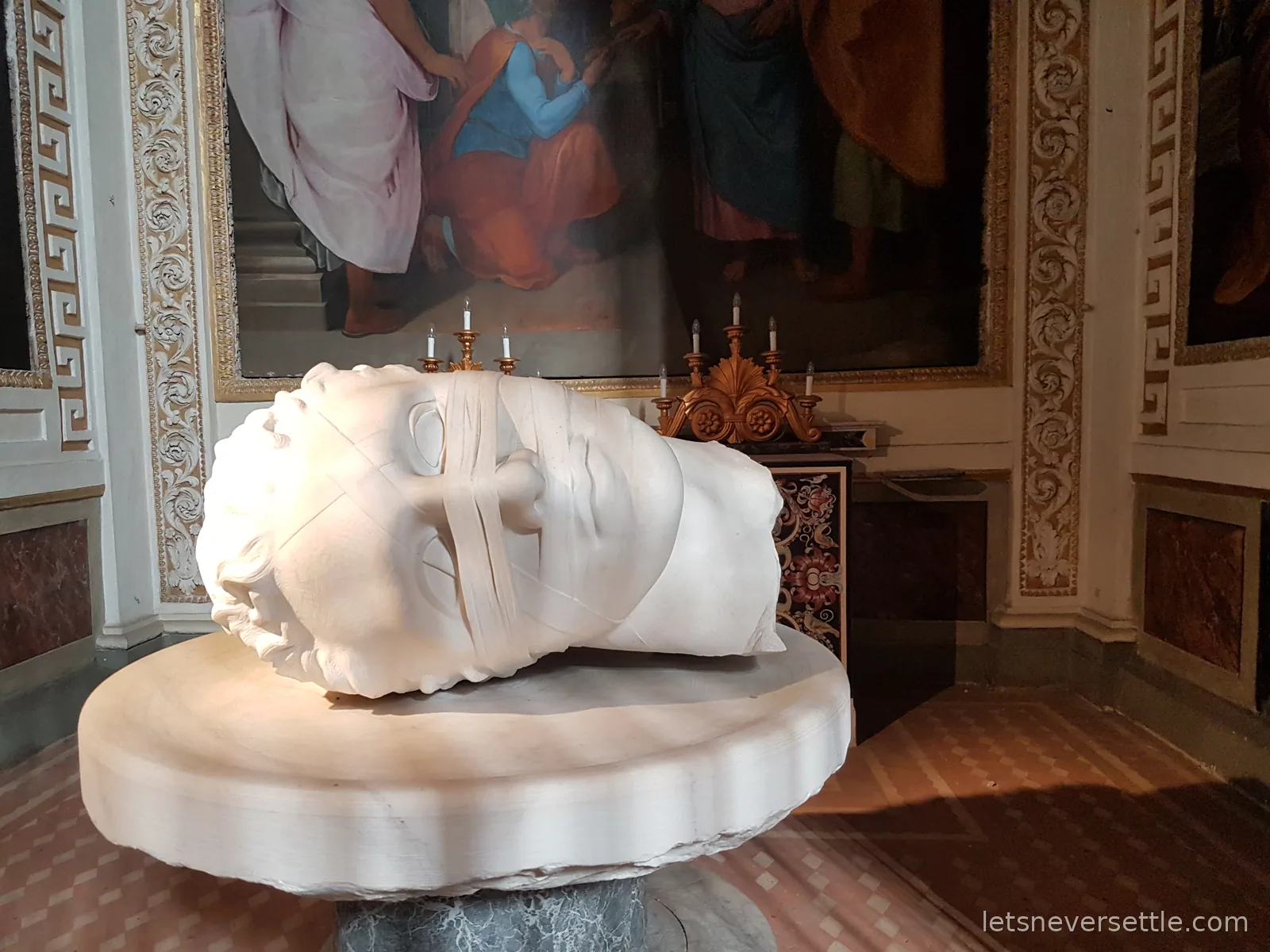 A colossal marble head lying on its side on a round marble base in a frescoed room