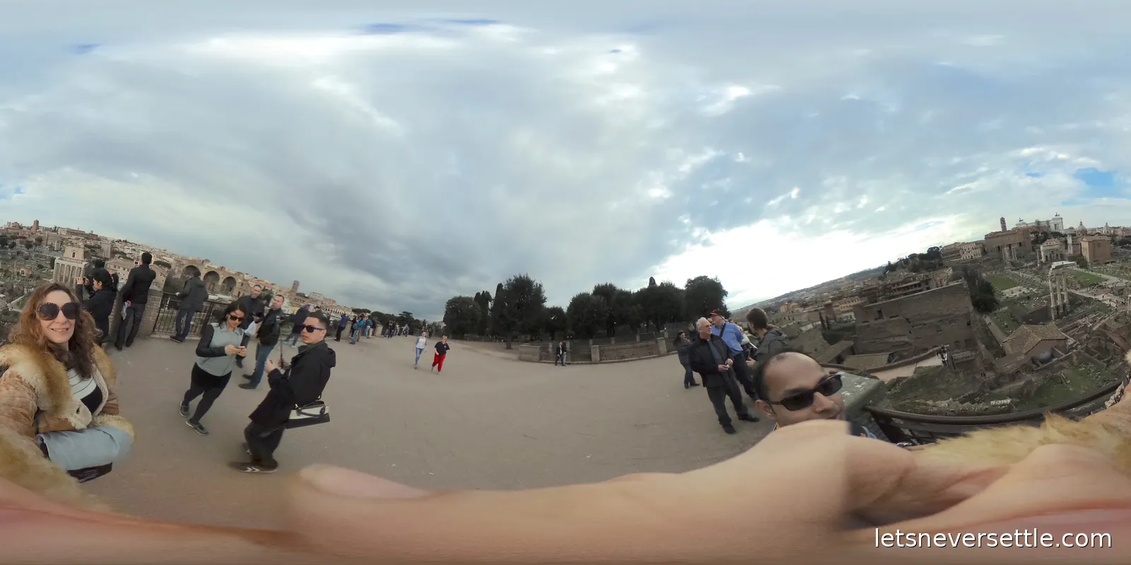 A wide gravel terrace crowded with visitors, with the columns and roofs of the Roman Forum dropping away on one side