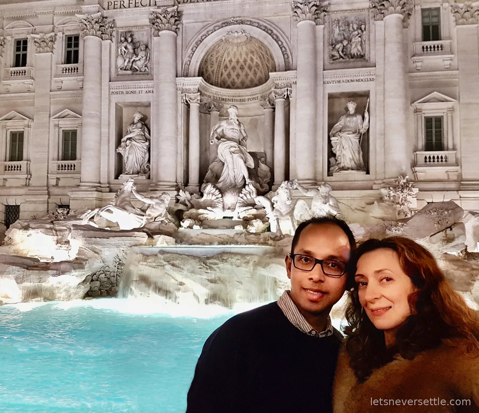Inga and Dileep in front of the floodlit Trevi Fountain at night, its water lit bright turquoise