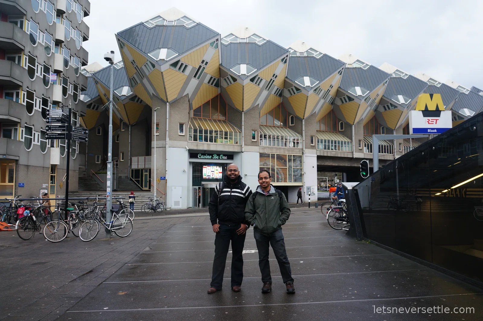 Dileep and his brother standing side by side outside Blaak metro station in Rotterdam with the cube houses rising behind them