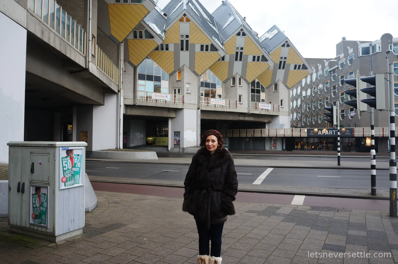 Inga in a dark fur coat standing on the pavement in front of the yellow cube houses at Blaak, Rotterdam
