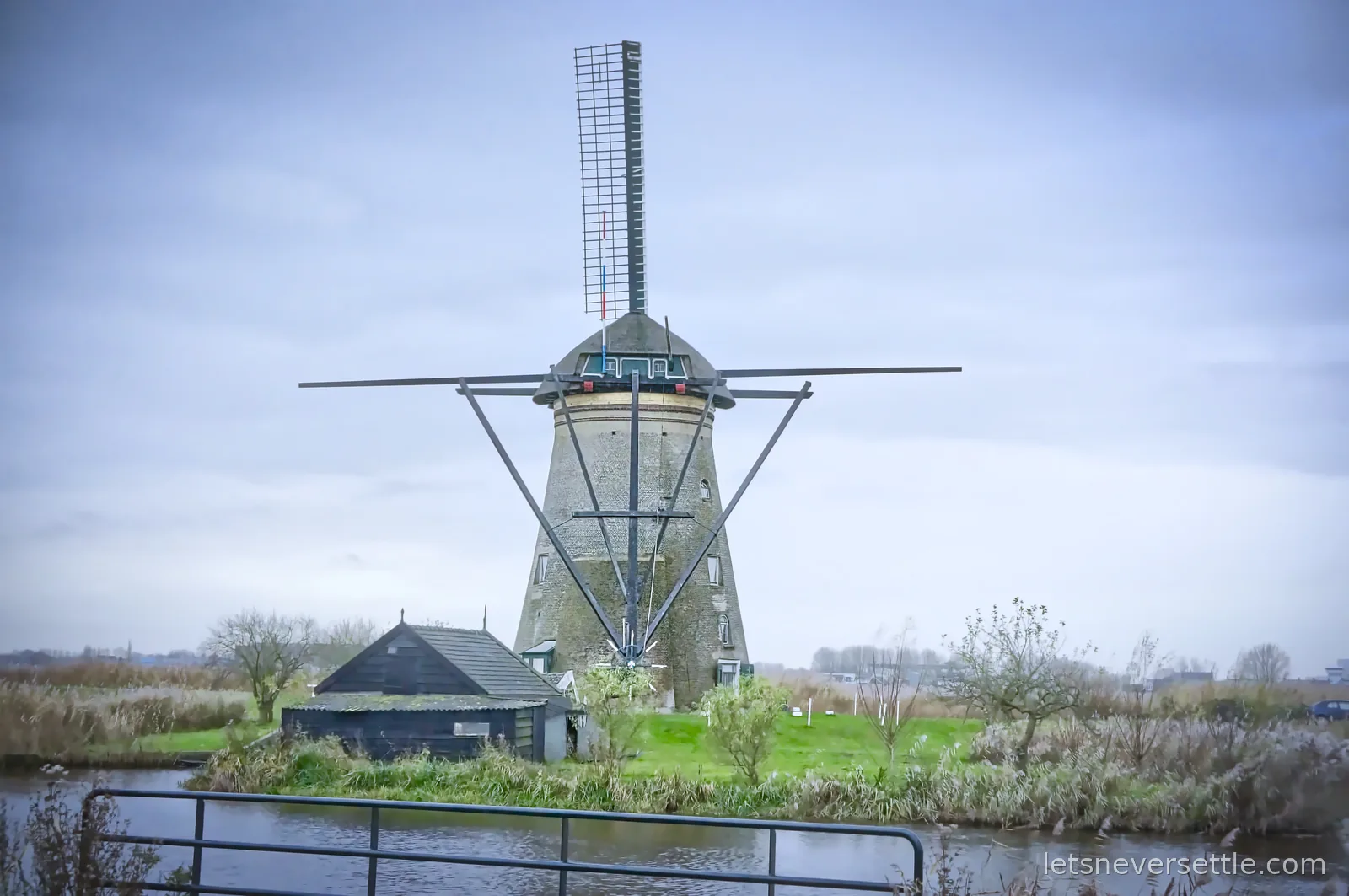 A brick smock windmill with a small wooden shed on the far bank of a canal at Kinderdijk