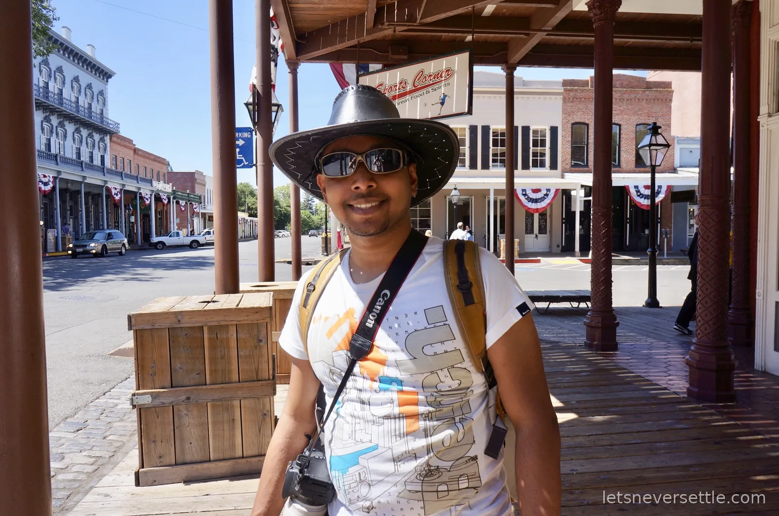 Dileep in a black cowboy hat under the wooden arcades of Old Sacramento, with brick Gold Rush era buildings and flag bunting along the street